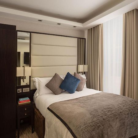 Montcalm Brewery Townhouse Hotel London Bagian luar foto The image shows a cozy bedroom. It features a comfortable double bed with a light-colored duvet and decorative pillows in shades of blue and gray. The headboard is upholstered in a soft material, and there are bedside lamps on either side of the bed.