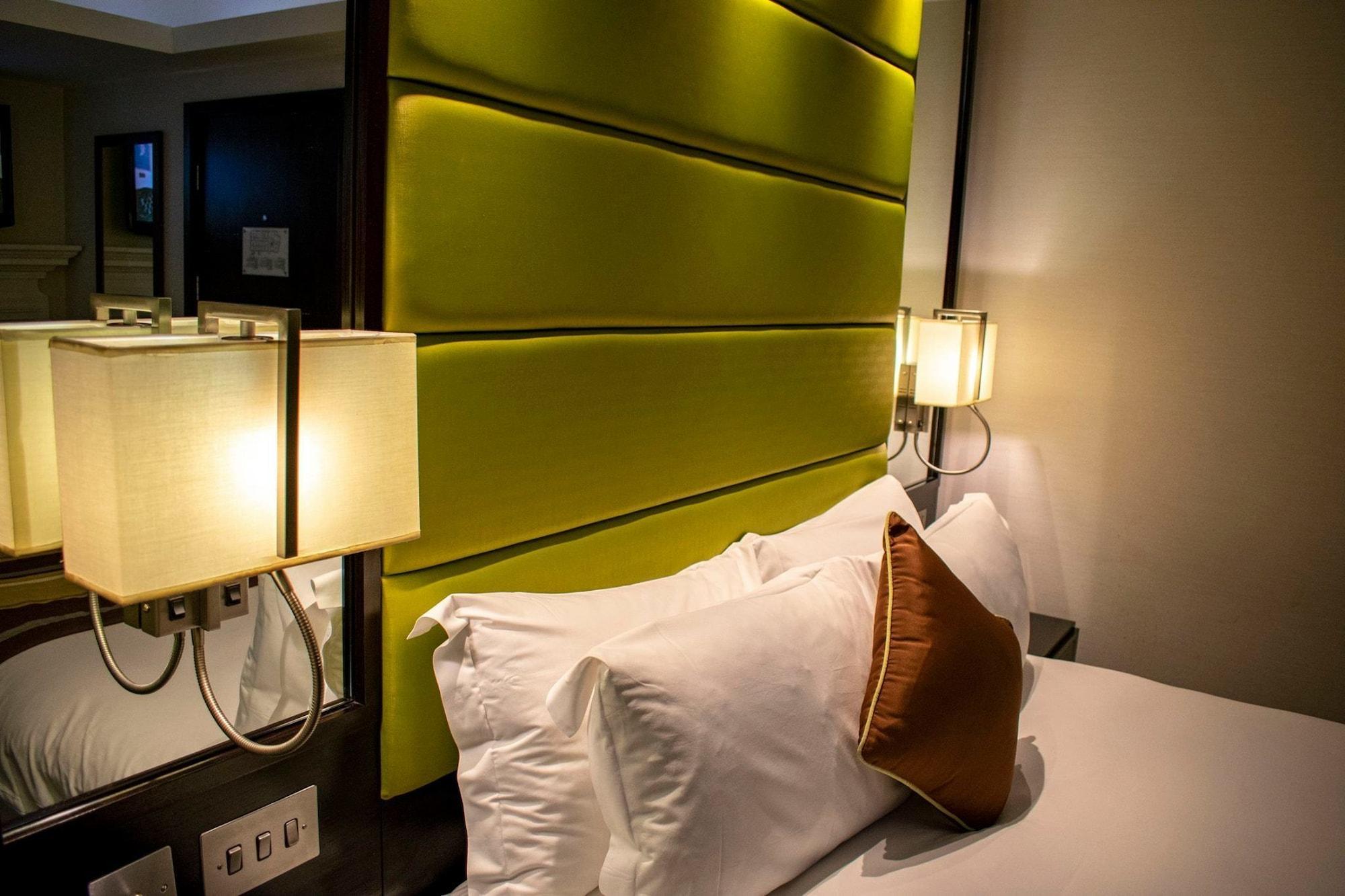 Montcalm Brewery Townhouse Hotel London Bagian luar foto The photo shows a modern hotel room with a stylish design. The focal point is a large bed with white pillows and a decorative brown pillow. The headboard is bright green and has a textured appearance. On either side of the bed, there are wall lamps t