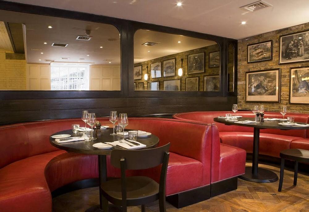 Montcalm Brewery Townhouse Hotel London Bagian luar foto The image shows the interior of a restaurant featuring a warm and inviting atmosphere. There are several round tables surrounded by black chairs, with red, upholstered booths lining the walls. The decor includes framed artwork hanging on the walls, a