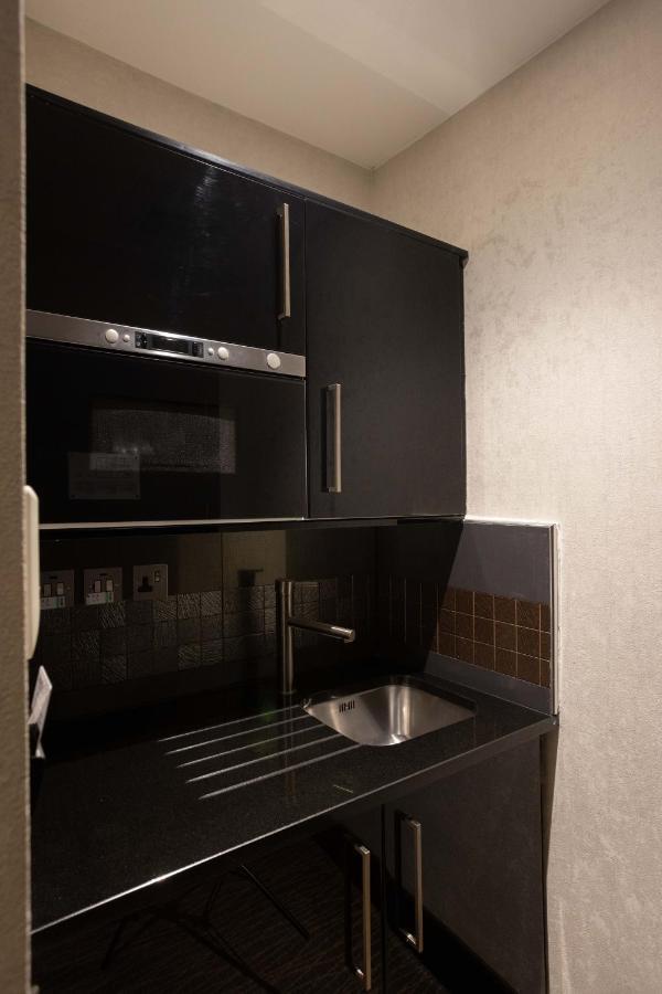 Montcalm Brewery Townhouse Hotel London Bagian luar foto The photo shows a modern kitchen setup with a dark color scheme. It features:

- A built-in microwave oven situated above a countertop.
- A sleek black cabinet beneath the microwave, which likely stores kitchen items.
- A stainless steel sink placed 