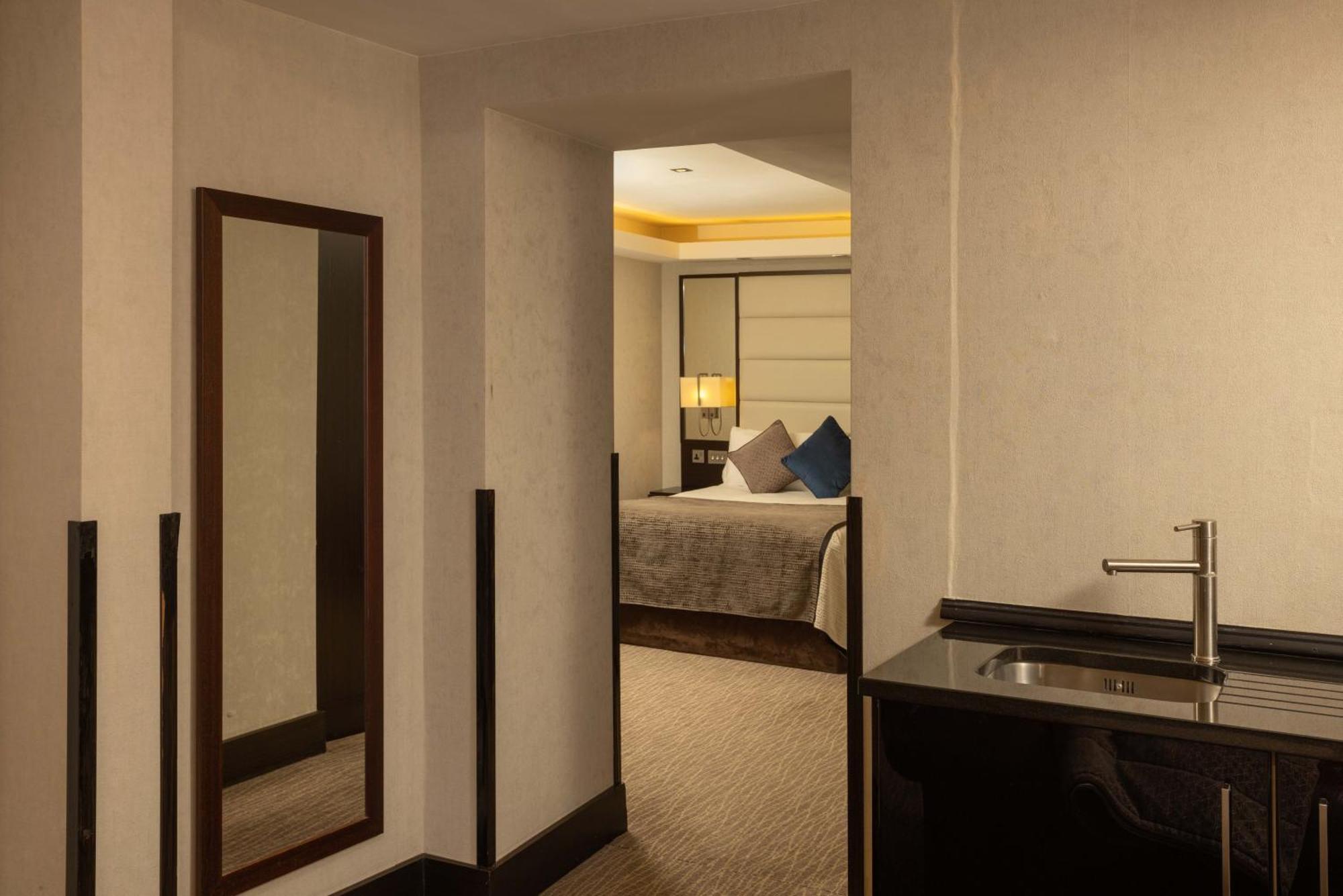 Montcalm Brewery Townhouse Hotel London Bagian luar foto The photo shows an interior space that appears to be part of a hotel room or suite. There is a doorway leading into a bedroom area, where a bed with decorative pillows is visible. In the foreground, there's a tall mirror on the left side and a small 