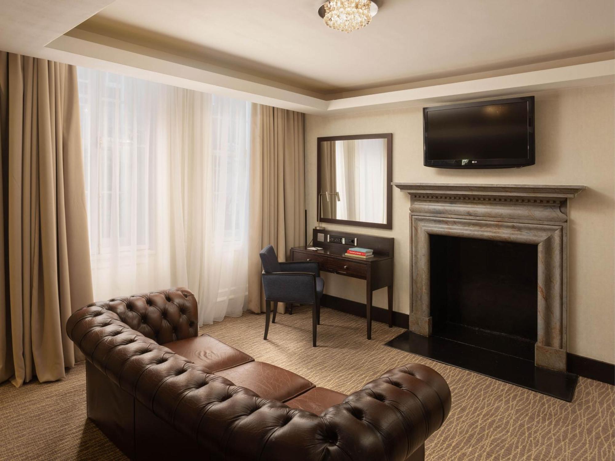 Montcalm Brewery Townhouse Hotel London Bagian luar foto The photo shows a cozy and elegantly designed room. There is a comfortable brown leather sofa with tufted detailing. A small desk and chair are positioned near a mirror, providing a space for work or personal grooming. On the wall, a flat-screen TV i