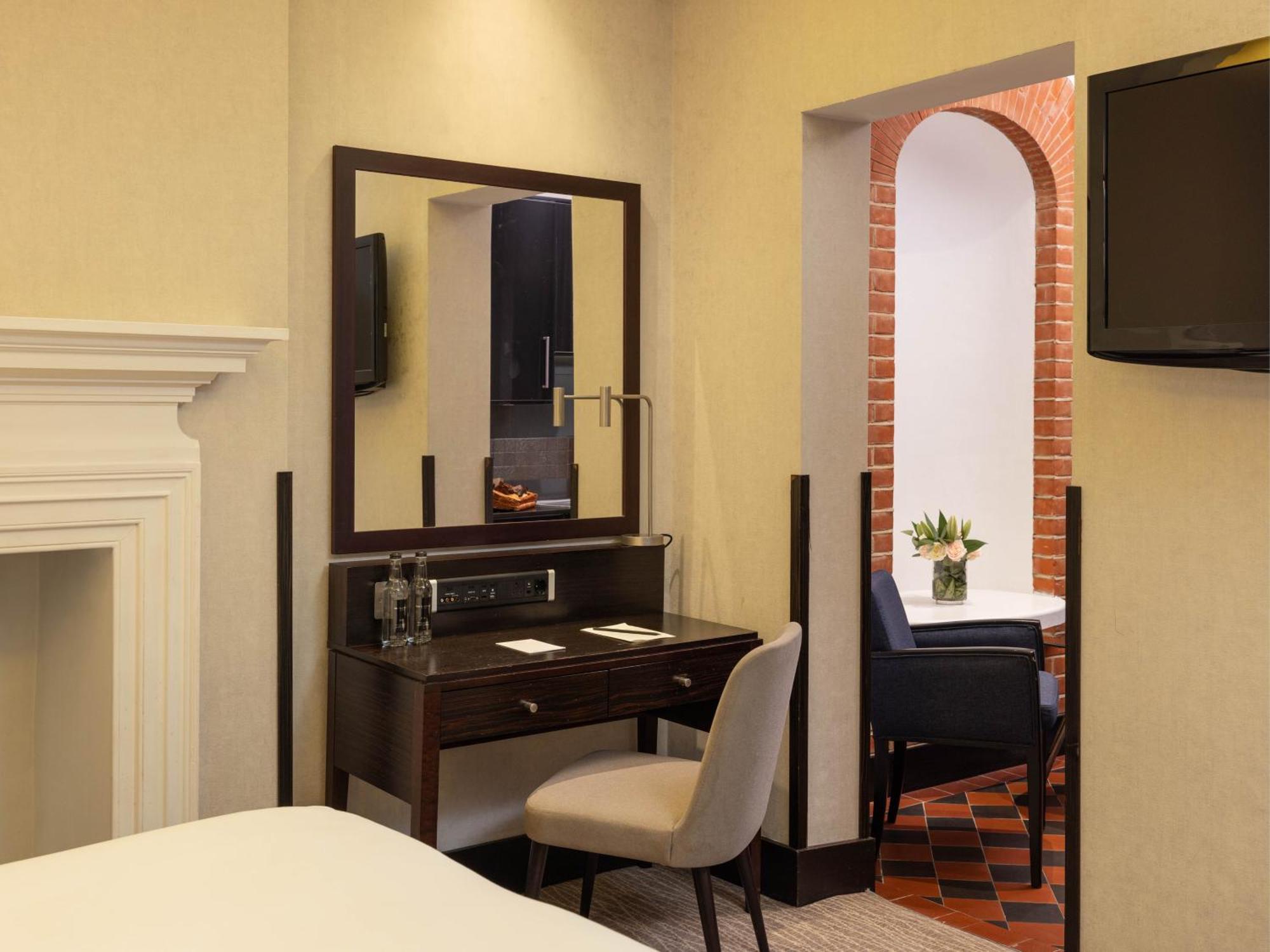 Montcalm Brewery Townhouse Hotel London Bagian luar foto The photo displays a hotel room setup. On the left side, there's a bed with a simple white bedding arrangement. Adjacent to the bed, there's a wooden desk with a chair, along with a mirror above the desk. The desk area is equipped with some glassware