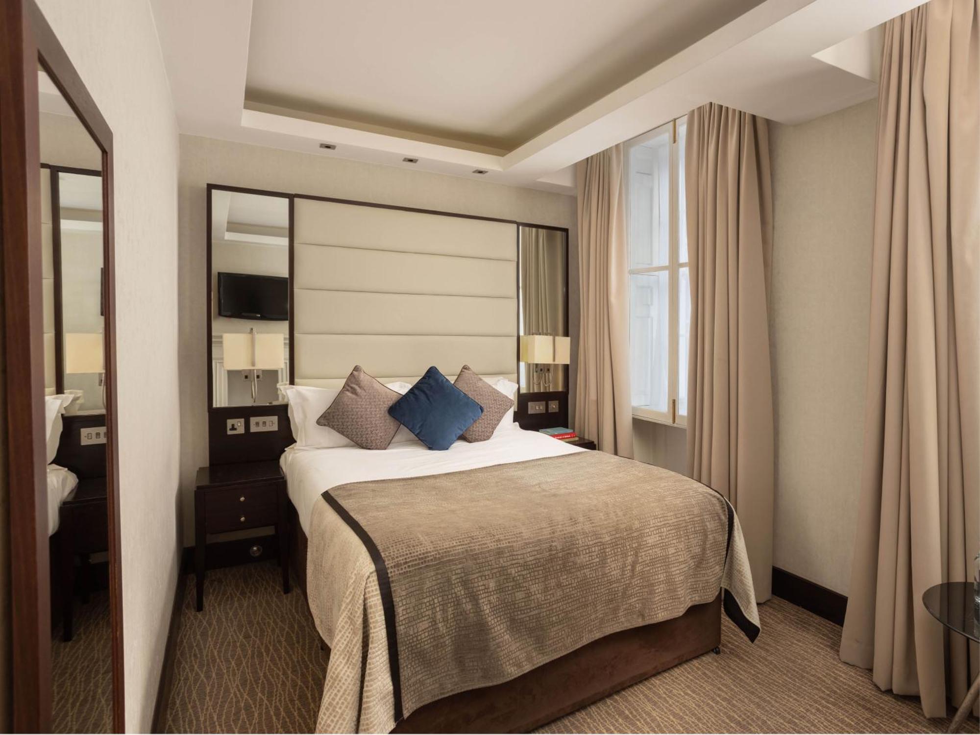 Montcalm Brewery Townhouse Hotel London Bagian luar foto The photo shows a cozy hotel room with a bed as the focal point. The bed is made with neutral-colored linens and has several pillows, including a decorative blue one. There are bedside tables on either side of the bed, each with a lamp. A large mirro