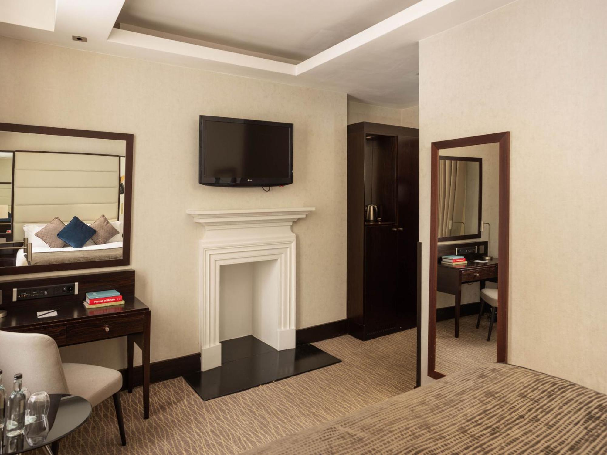 Montcalm Brewery Townhouse Hotel London Bagian luar foto The photo depicts a stylish hotel room. It features a double bed, a large flat-screen TV mounted on the wall, and a decorative fireplace. There is a wooden desk with a chair beside it, as well as a mirror hanging on the wall. The decor is modern and 
