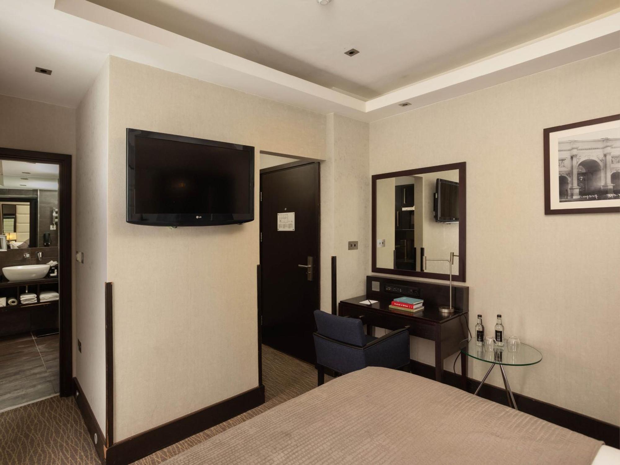 Montcalm Brewery Townhouse Hotel London Bagian luar foto The photo shows a hotel room with a modern and minimalist design. On the left, there's a wall-mounted flat-screen TV. In the center, there's a bed with a neutral-colored bedspread. To the right of the bed, there is a small desk with a mirror above it