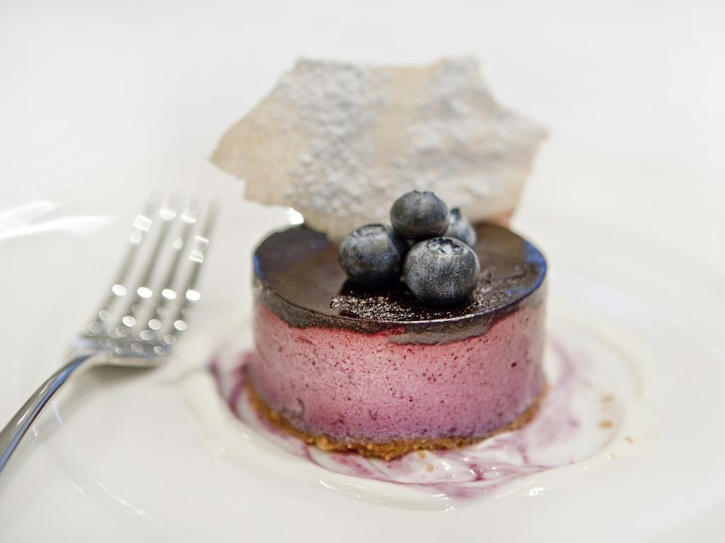 Montcalm Brewery Townhouse Hotel London Bagian luar foto The photo shows a beautifully plated dessert, which appears to be a round cheesecake or mousse. It has a pinkish-purple filling, topped with a glossy dark chocolate layer. Three fresh blueberries sit on top, adding a pop of color. The dessert is acco